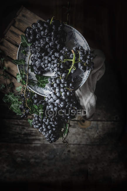 Bunch of fresh grapes on vintage plate on wooden table — Stock Photo