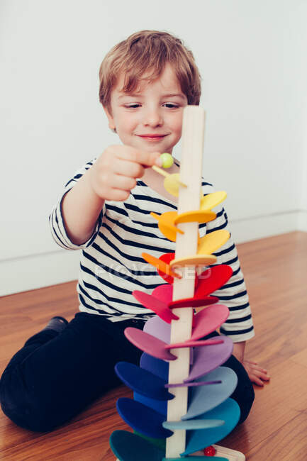 Funny smiling kid playing with toy tower and sitting on floor in room — Stock Photo
