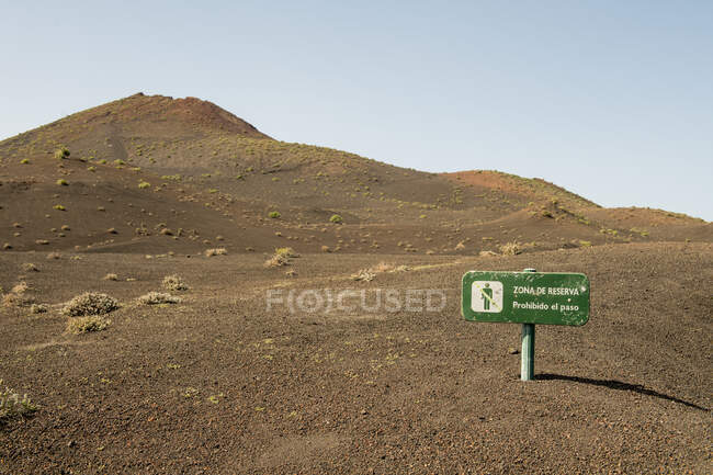 Маленький знак предосторожности расположен на каменистой земле возле красивого холма в солнечный день на природе — стоковое фото