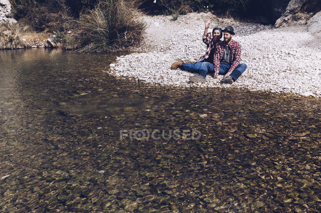 Side view of young couple lying on rock coast of mountain river near cliff — Stock Photo