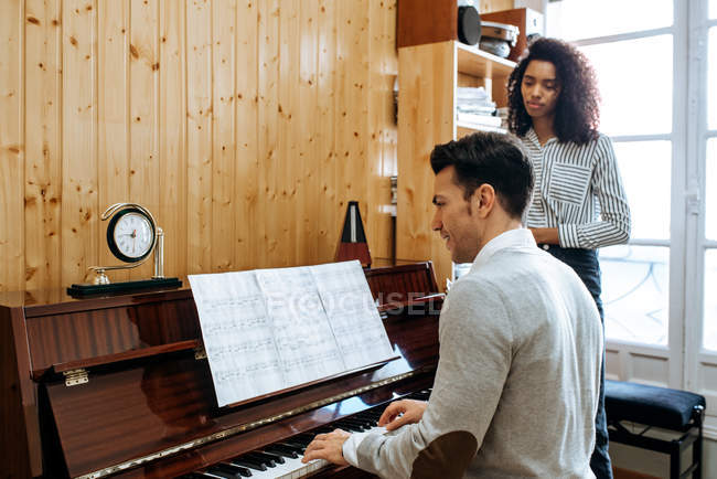 Young man learning to play piano near black woman teaching in music studio — Stock Photo