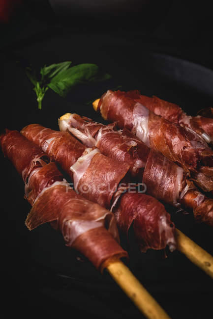 Gressini con tipico prosciutto serrano spagnolo su piatto nero — Foto stock