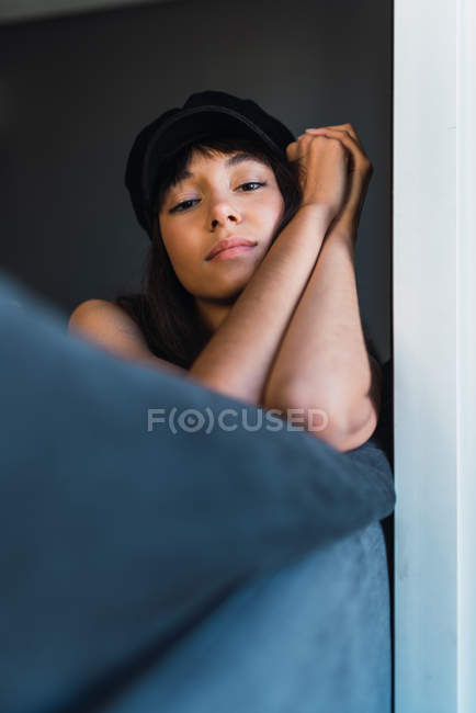 Attraente giovane donna elegante in berretto guardando la fotocamera mentre riposava sul divano — Foto stock