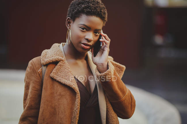 Афро-американская элегантная женщина разговаривает по мобильному телефону и смотрит в камеру на улице — стоковое фото