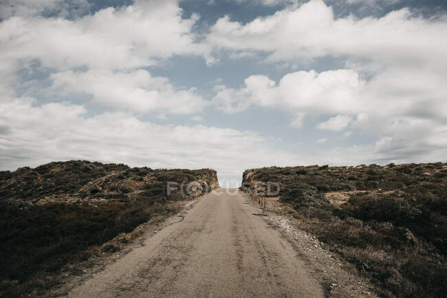 Nuvens brancas bonitas flutuando no céu azul sobre colina áspera com estrada de campo estreita — Fotografia de Stock