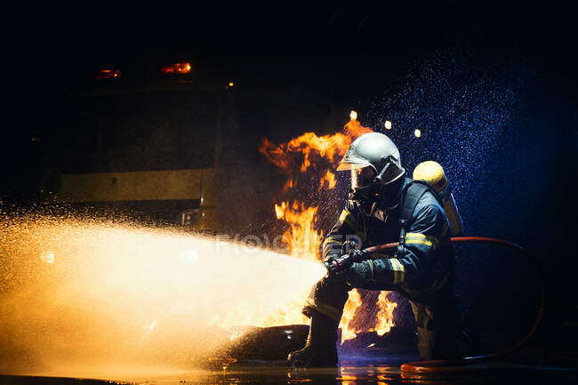 Homem irreconhecível em uniforme de bombeiro suprimindo fogo com fluxo pesado de água — Fotografia de Stock