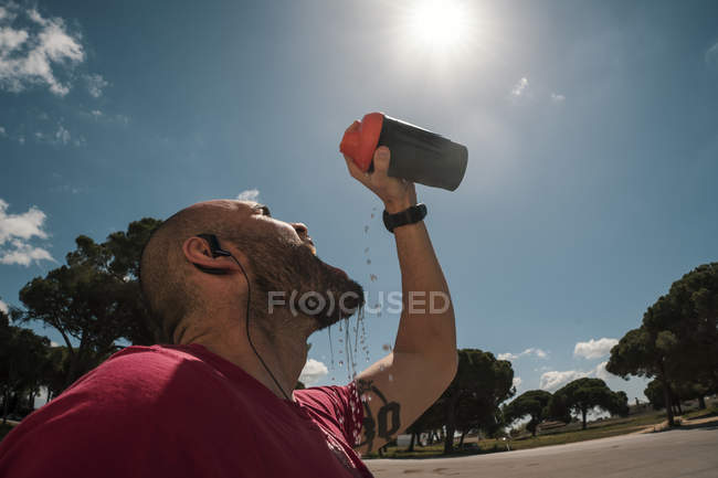 Человек пьет во время тренировки против голубого неба с облаками — стоковое фото