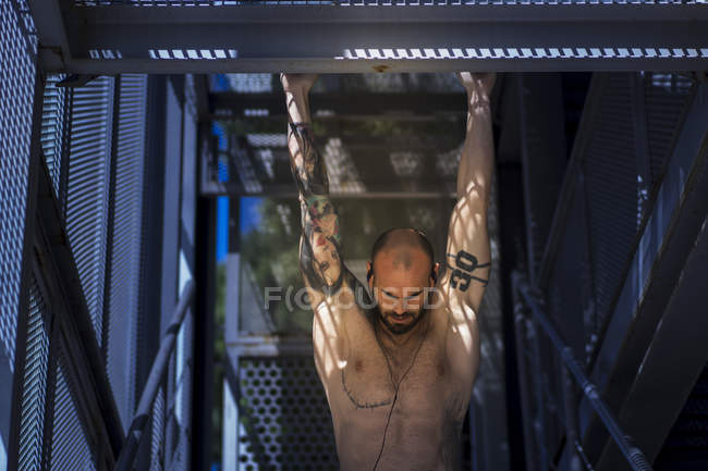 Muscular guy performing pull ups in stairway — Stock Photo