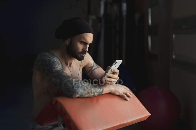 Без рубашки татуированный спортсмен со смартфоном в тренажерном зале — стоковое фото