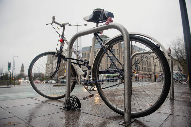 Bicicleta moderna situada cerca del estante de estacionamiento de metal en la calle húmeda en el día lluvioso en Londres - foto de stock