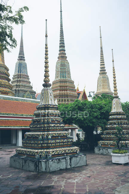 Ornamental pyramids decorating yard of amazing oriental temple against gray sky in Thailand — Stock Photo