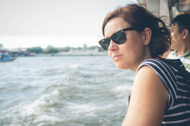 Vista laterale della femmina in occhiali da sole guardando il mare tempestoso mentre si viaggia su una nave moderna in Thailandia — Foto stock