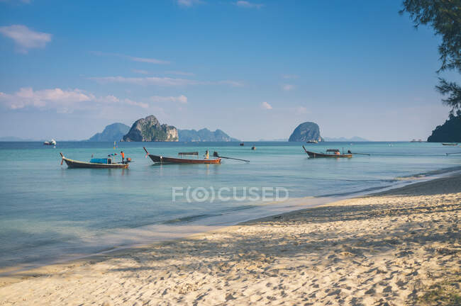 Piccole barche galleggianti su acque calme vicino alla riva sabbiosa nella giornata di sole in Thailandia — Foto stock