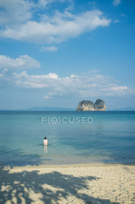 Вид сзади на далекую женщину, сидящую в спокойной голубой морской воде в солнечный день в Таиланде — стоковое фото