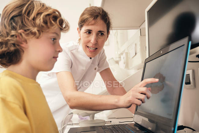 Female dentist demonstrating teeth scan on laptop screen to boy in modern clinic — Stock Photo
