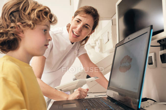 Dentiste femme démontrant balayage des dents sur écran d'ordinateur portable pour garçon dans la clinique moderne — Photo de stock