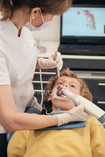 Donna in maschera e uniforme medico fare la scansione dei denti del bambino mentre si lavora in clinica dentista — Foto stock
