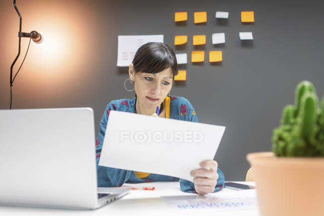 Mujer de negocios que trabaja con documentos mientras está sentada en el escritorio en la oficina moderna - foto de stock