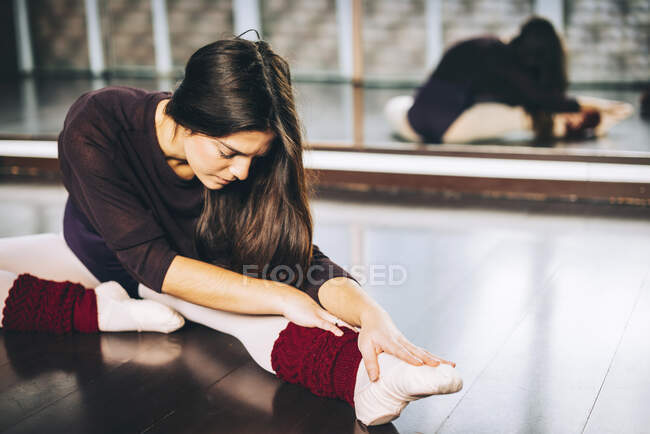 Девушка практикует балет и сгибает мышцы сидя на полу в студии. — стоковое фото