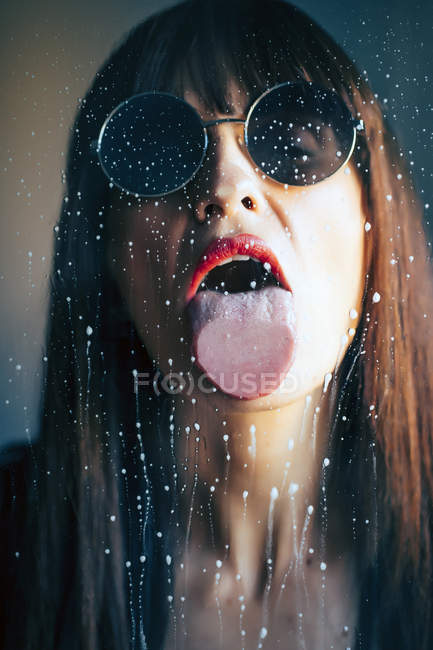 Mulher atraente com batom vermelho lambendo gotas líquidas de vidro transparente — Fotografia de Stock