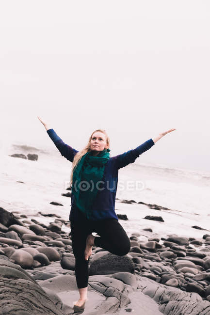 Молодая женщина с поднятыми руками медитирует и стоит на скалах возле морского побережья — стоковое фото