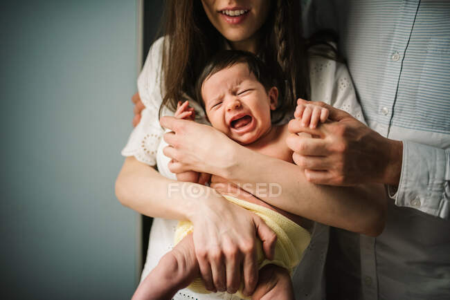 Homme et femme anonymes embrassant et réconfortant pleurant bébé nouveau-né dans une chambre confortable à la maison — Photo de stock