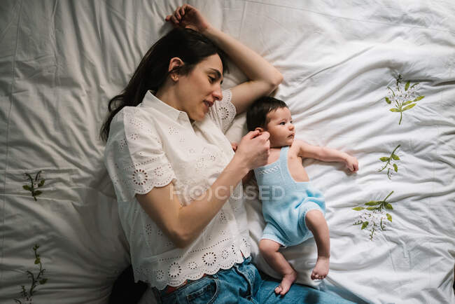 Красива доросла жінка ніжно торкається солодкої дитини, лежачи на зручному ліжку разом — стокове фото