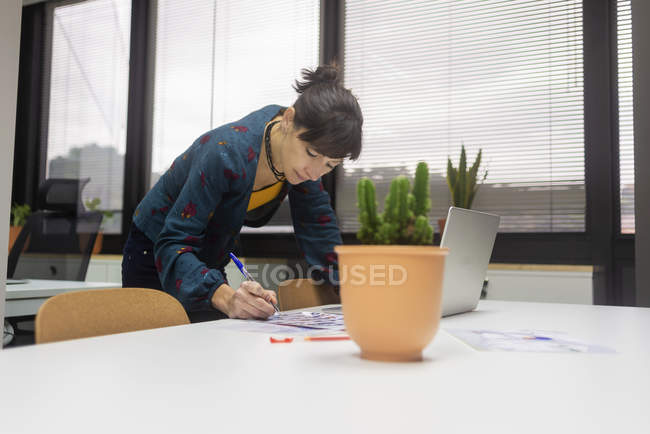 Бізнес-леді, що працює з документами, стоячи за столом в сучасному офісі — стокове фото