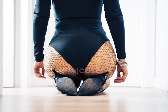 Rückansicht einer provokanten Frau mit perfektem Gesäß, die erotischen Body und Netzstrumpfhose trägt und auf dem Boden sitzt — Stockfoto