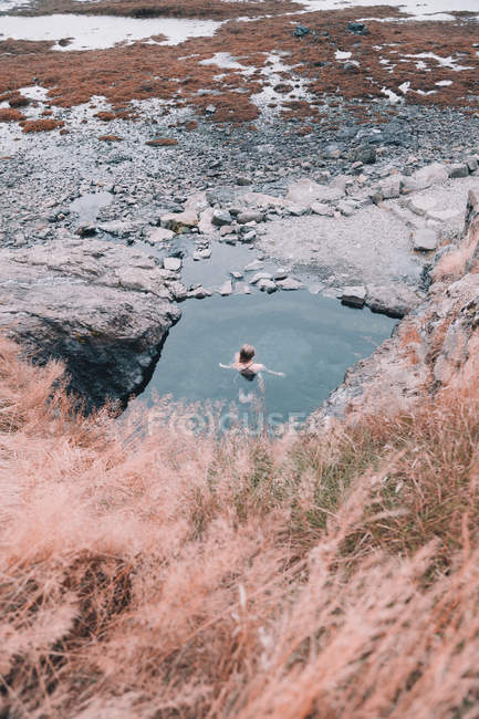 Woman resting in water near cliff on dry coast between stones — Stock Photo