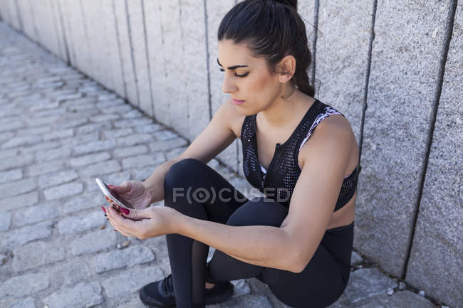 Morena mujer sentado y comprobar la aplicación de entrenamiento - foto de stock