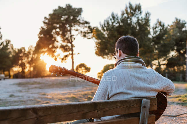Mann sitzt auf Bank in der Natur und spielt Gitarre — Stockfoto