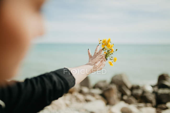 Main de femme jetant de petites fleurs jaunes dans l'eau de mer le jour ensoleillé — Photo de stock