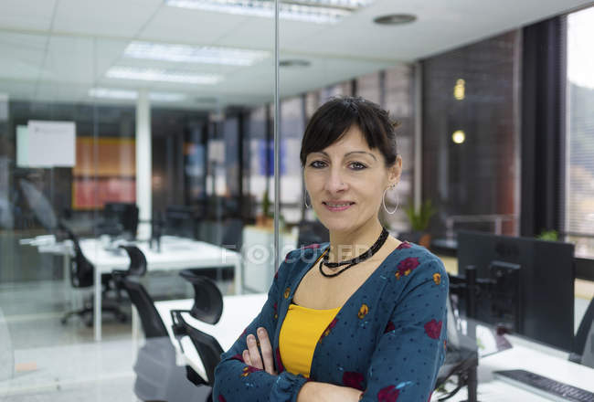 Porträt einer lächelnden Managerin, die an einer Glaswand in einem modernen Büro steht — Stockfoto