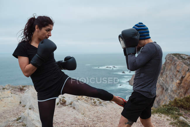 Мужчина и женщина в боксёрских перчатках бьют друг друга, стоя на скале у моря и неба — стоковое фото