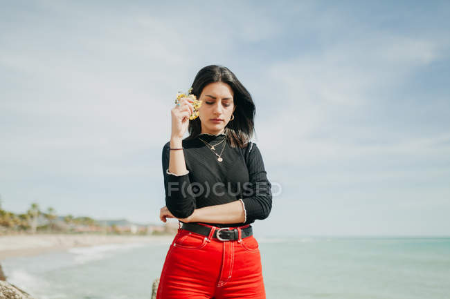 Sensual young woman with bunch of yellow flowers standing near sea on sunny day — Stock Photo