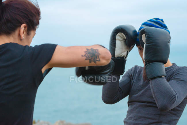 Hombre y mujer en guantes de boxeo golpeándose entre sí mientras están de pie contra el mar - foto de stock