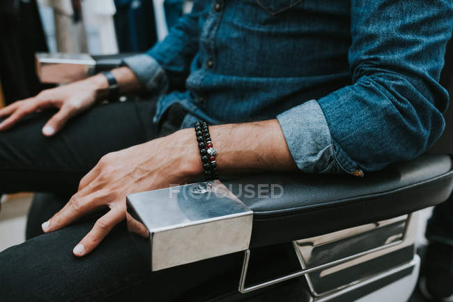 Vista laterale di uomo elegante con braccialetto a portata di mano seduto in sedia in salone — Foto stock