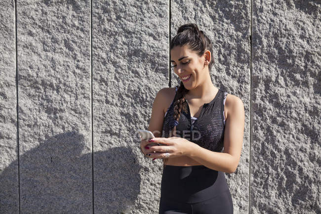 Mulher morena encostada à parede de granito enquanto usa telefone e rindo — Fotografia de Stock