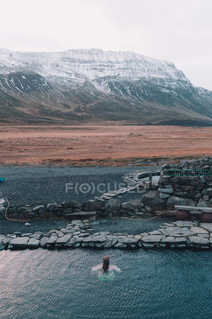 Вид женщины, плавающей в голубой воде природного водохранилища с горами на заднем плане — стоковое фото
