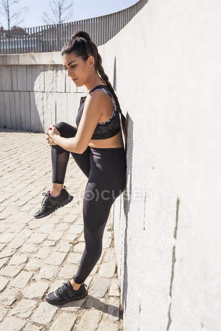 Femme brune étirant les muscles par une journée ensoleillée avec un mur de granit sur le fond — Photo de stock