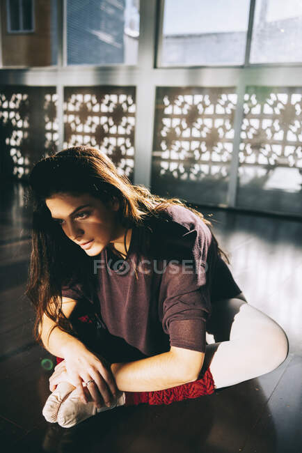 Молодая красивая женщина наклоняется вперед, растягивая ноги, сидя на студии в солнечном свете. — стоковое фото