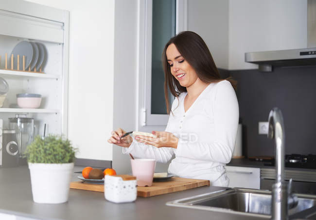 Jovem mulher feliz fazendo sanduíche à mesa na cozinha em casa — Fotografia de Stock