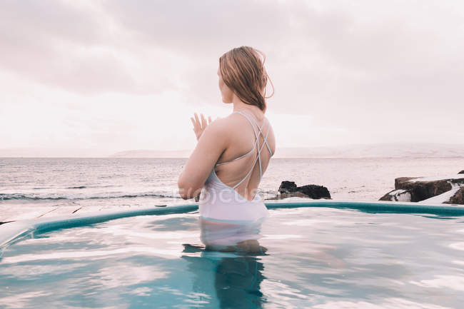 Молода жінка медитує у воді басейну біля каменів і хмарного неба. — стокове фото