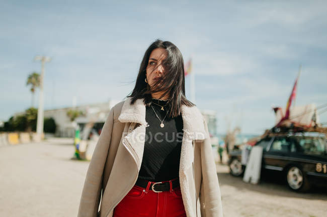 Jeune femme réfléchie en tenue tendance avec veste debout sur fond flou de parking de plage — Photo de stock