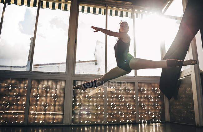 Junge schlanke Ballerina springt im Studio über den Boden und beugt die Beine. — Stockfoto
