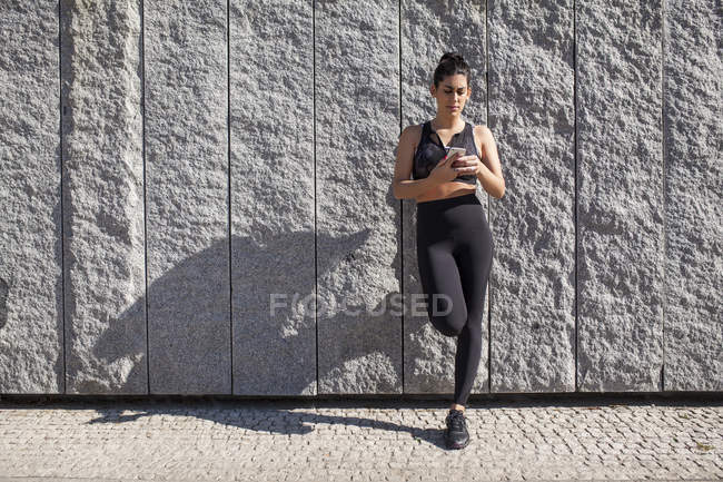 Morena mujer apoyada contra la pared de granito mientras usa el teléfono - foto de stock