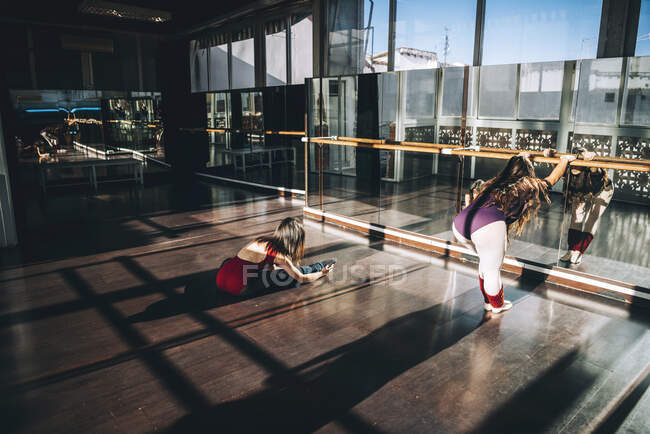 Jovens bailarinas trabalhando em espaçoso estúdio ensolarado aquecendo os músculos na frente do espelho. — Fotografia de Stock