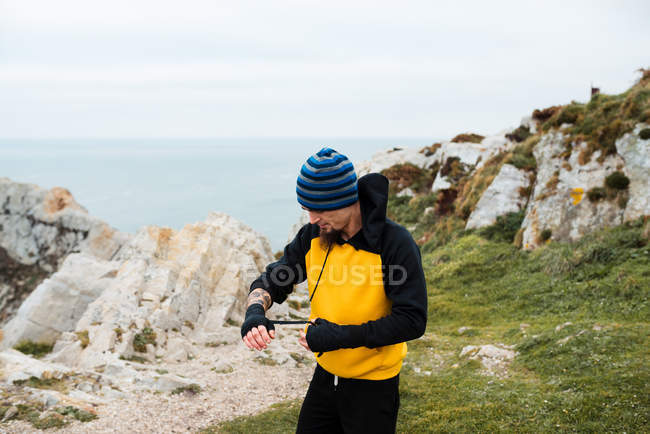 Bearded adult man wrapping bandage around hand while standing against sea during outdoor kickboxing training — Stock Photo