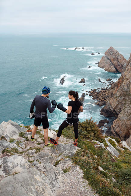 Uomo e donna in guantoni da boxe in piedi sulla scogliera contro il mare — Foto stock